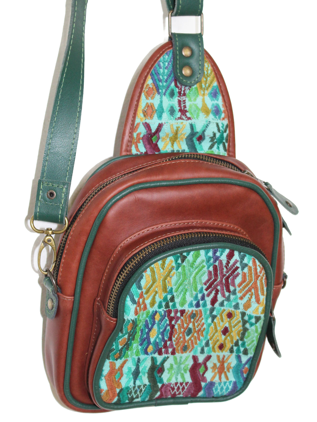 MoonLake Designs Blake Sling Over Backpack Bag in red brown (burnt sienna) with geometric huipil in shades of greens, blues, and complementary colors featuring dark green leather adjustable strap and multiple easy access pockets